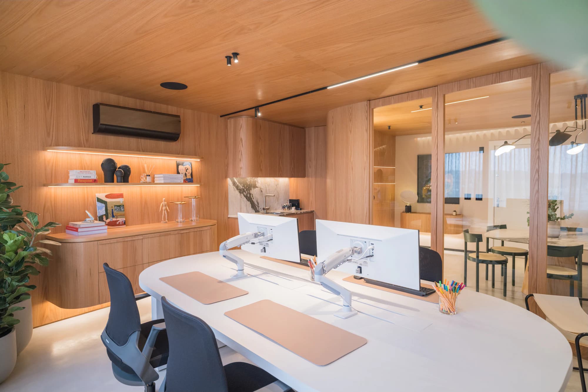 Workstations with monitors in an office lined with warm oak millwork and planting