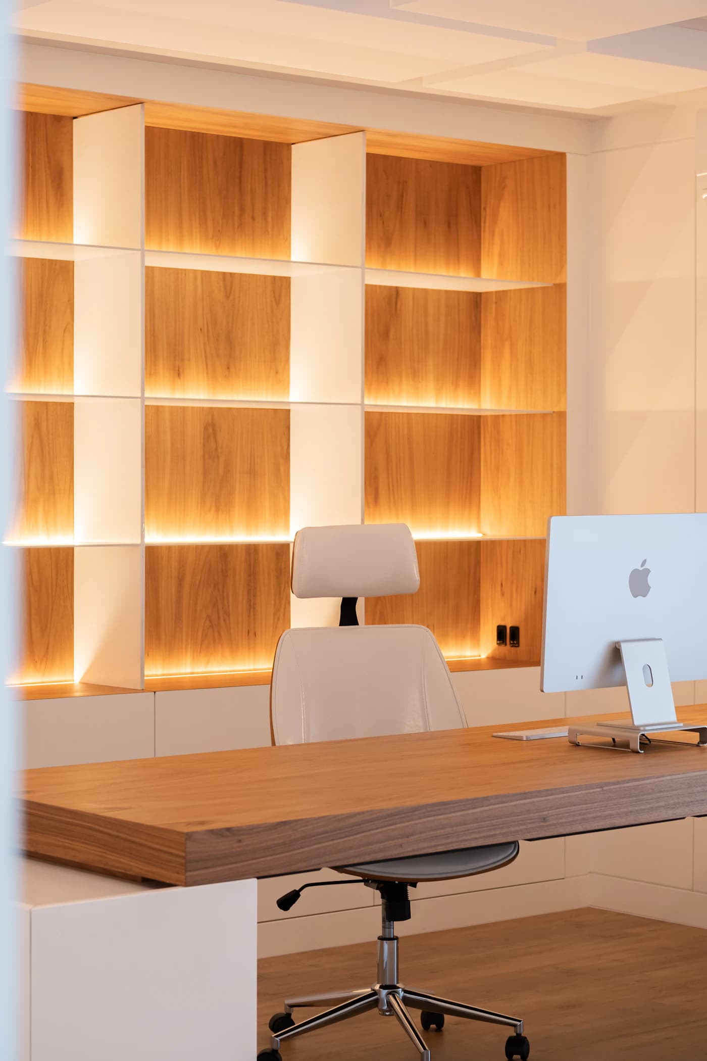 A desk beside backlit oak shelving in a finished office interior